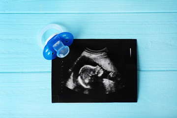 Ultrasound photo and pacifier on blue wooden background