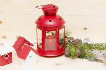 Red metal lantern has a burning candle. Holiday lamp is on the wooden background. 