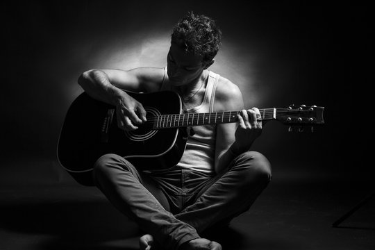 Young caucasian man play a acoustic guitar. Black and white picture, low key studio portrait