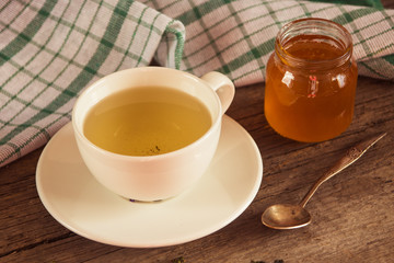 Green tea in a white cup and jar of honey with spoon and green k
