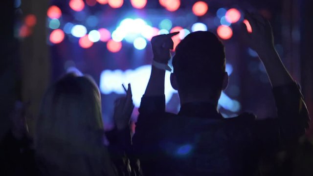 Energetic couple dancing and waving hands at cool music festival in night club
