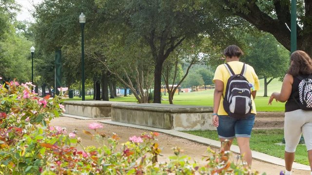 Two Overweight People Walking on a Path in Houston Texas Hermann Park during the Summer with Flowers and Green Foliage