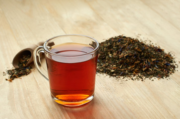 Glass cup of tea on the pile  dried  herbs  the wooden background.