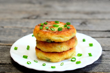 Fried vegetable patties on a plate. Yummy patties made of potatoes, green peas, carrot and green beans and garnished with fresh green onion. Veggie lunch or dinner idea. Vintage style. Closeup