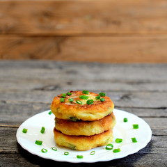 Mixed vegetable patties on a plate isolated on wooden background. Fried patties cooked of potatoes, green peas, carrot and green beans and garnished with fresh green onion. Delicious vegetable dish
