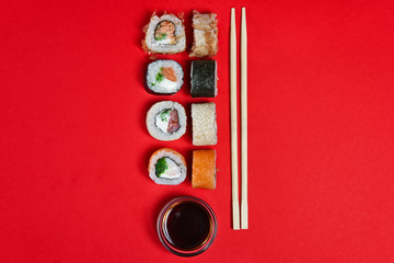 Set of salmon rolls, soy sauce and chopsticks on red background