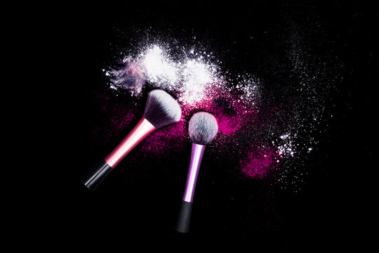 Makeup brushes with powder spilled glitter dust on black background. Pink powder on black table.