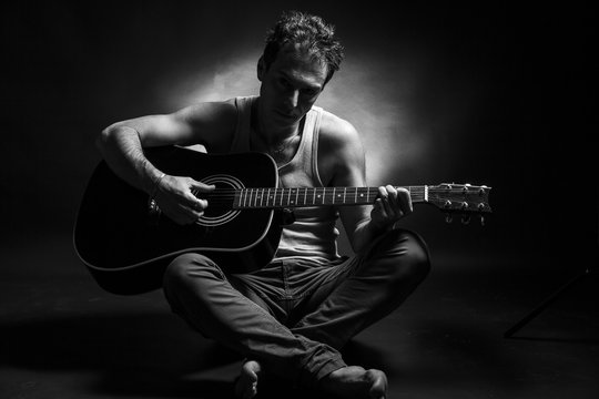 Young caucasian man play a acoustic guitar. Black and white picture, low key studio portrait