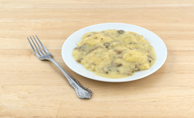 Ravioli in a cheese and mushroom sauce meal atop a wood table.