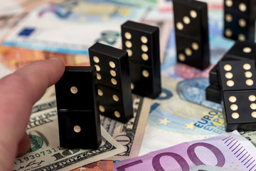 Finger pushing domino standing on euro and dollar cash.