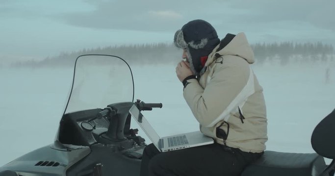 Young programmer who using notebook on snowmobile in adverse winter conditions. He is blowing into his hands to warm up. Yamal 2016 Red Epic 4k