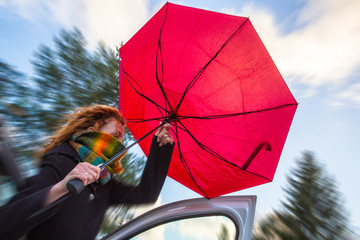 an einem stürmischen Tag versucht eine Frau einen Regenschirm aufzuspannen - obrazy, fototapety, plakaty