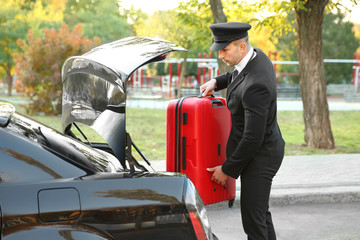 Chauffeur putting suitcase in car trunk