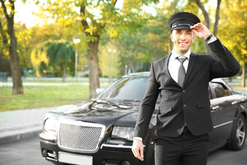 Young chauffeur adjusting hat near luxury car on the street - obrazy, fototapety, plakaty