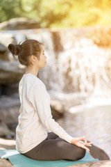 asian woman practices yoga at the waterfall