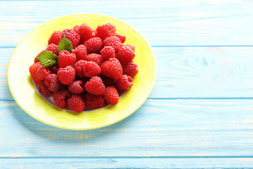 Red raspberries in plate on a blue wooden table