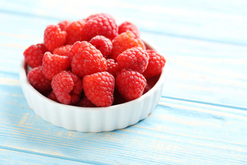 Fototapeta na wymiar Red raspberries in bowl on a blue wooden table