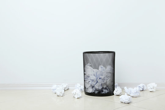 Office trashcan with crumpled paper balls on grey background
