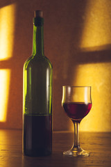 red wine glass near bottle on golden background and wood table