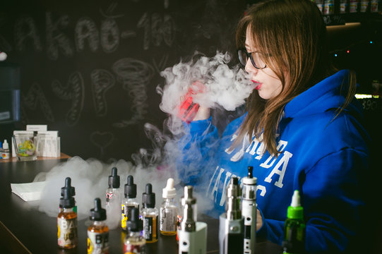 young Cute woman, the seller in vape shop shop, smoking electronic cigarette,  vaping and releases a cloud of vapor