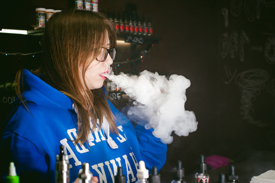 young Cute woman, the seller in vape shop shop, smoking electronic cigarette,  vaping and releases a cloud of vapor
