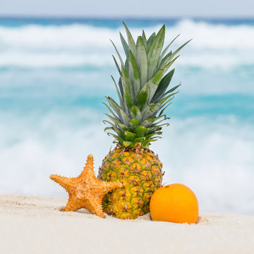 Pineapple, orange fruit and starfish on sand against turquoise c