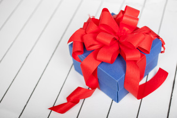 Blue gift box with red ribbon and bow on wooden background