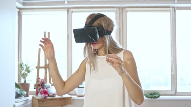 Slow motion of blonde woman in white space trying virtual reality glasses.