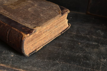 Old leather bound book laying on a dusty wooden bookshelf