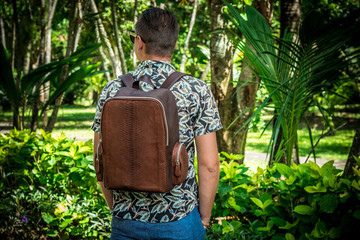 Tourist with stylish brown snakeskin python backpack in the asian park. Bali, Indonesia. Handsome...