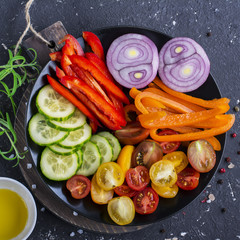 Ingredients for fresh vegetable salad tomatoes, cucumbers, sweet peppers on a dark background with salt, olive oil and herbs. Top view