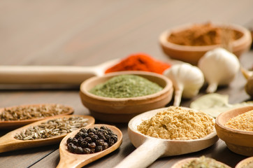 Different spices in bowls and wooden spoons on the table
