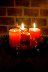 Four red candles with christmas decoration in atmospheric light. Moody. Authentic.