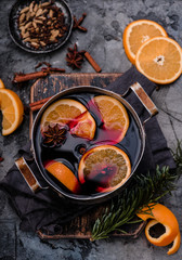 Mulled wine with orange and spices in aluminum vintage casserole on wooden board. Concrete background. Hot drink. Top view.