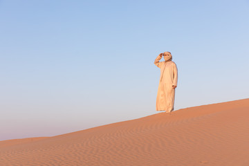 Fototapeta na wymiar Man in a traditional arab dress in desert at sunrise. Dubai, UAE.