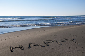Word happy handwritten on sand