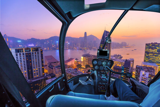 Helicopter Cockpit Flying Aerial View Of Victoria Harbor, Skyscrapers And Hong Kong Skyline At Night.