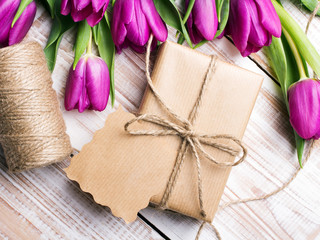 Gift box and tulips bouquet on white wooden background - retro style