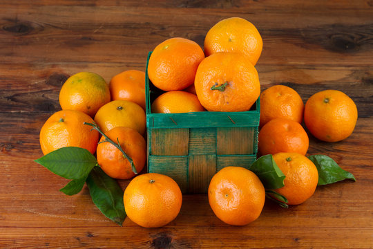 tangerine mandarin fruits in green basket on brown wooden background
