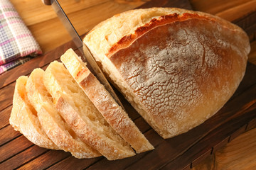 Slicing of fresh bread on wooden cutting board closeup