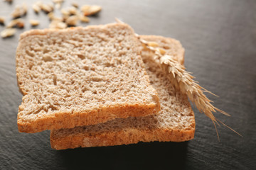 Sliced fresh bread with wheat spike on black table closeup