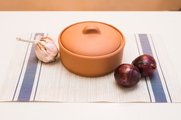clay pot, garlic and red onions on the table