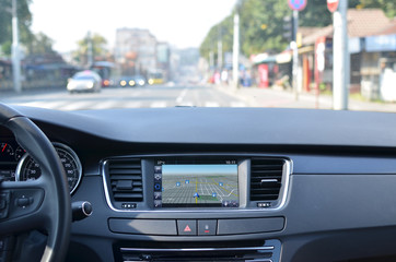 View from inside a car on a part of dashboard with a navigation unit and blurred street in front of...