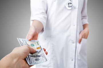 Patient is giving money to a doctor in hospital, gray background