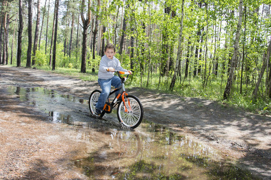 In the summer in the woods a little boy rides through a puddle o