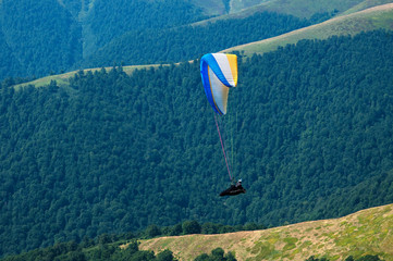 Paraglider flying over the picturesque mountains on a sunny summer day