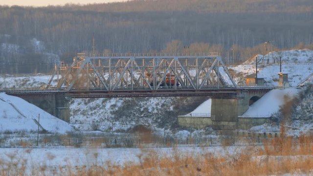 Working locomotive passes through a railway bridge. Winter landscape