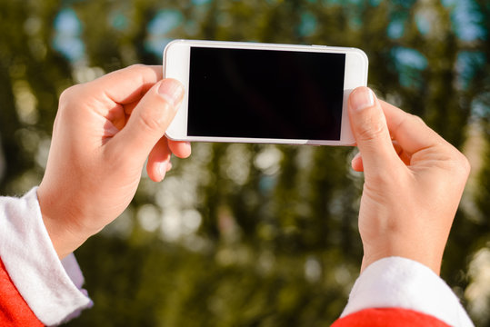 Santa Claus holding using mobile smartphone ready for Christmas time on green fir background