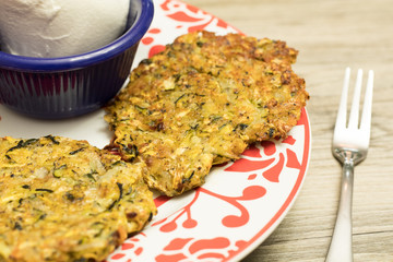 Homemade baked zucchini pancakes on a festive red and white plate served with sour cream