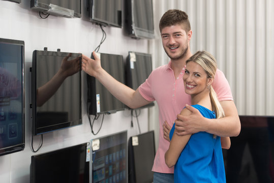 Smiling Couple Buying A Television In Supermarket